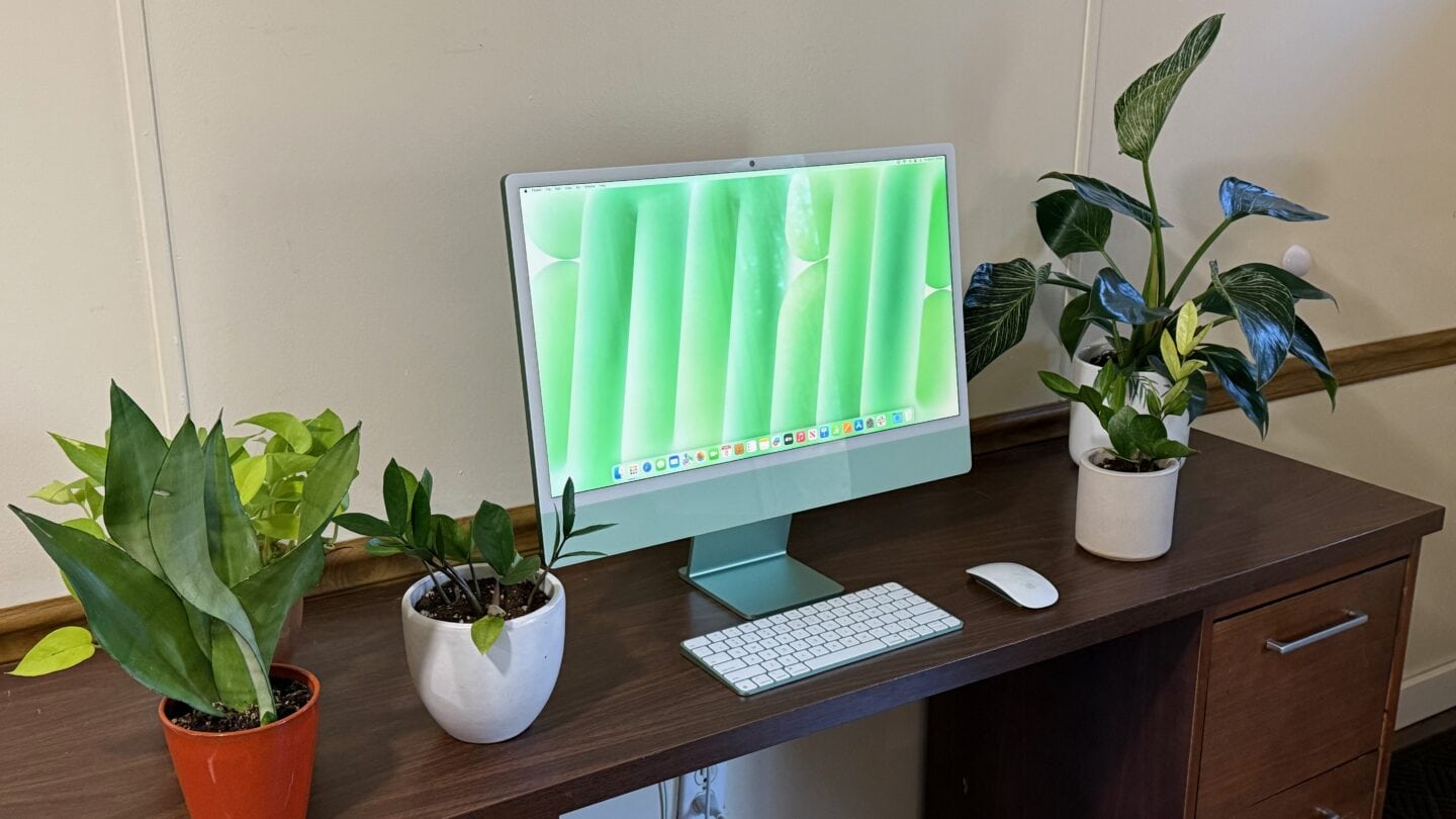 Green iMac sitting on a brown desk with various potted plants around it