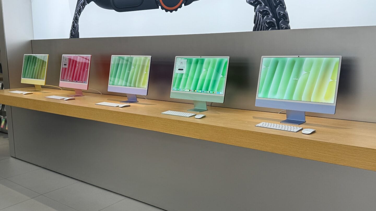 A line of five M4 iMacs in an Apple Store. From left to right, Yellow, Pink, Purple, Green and Blue.