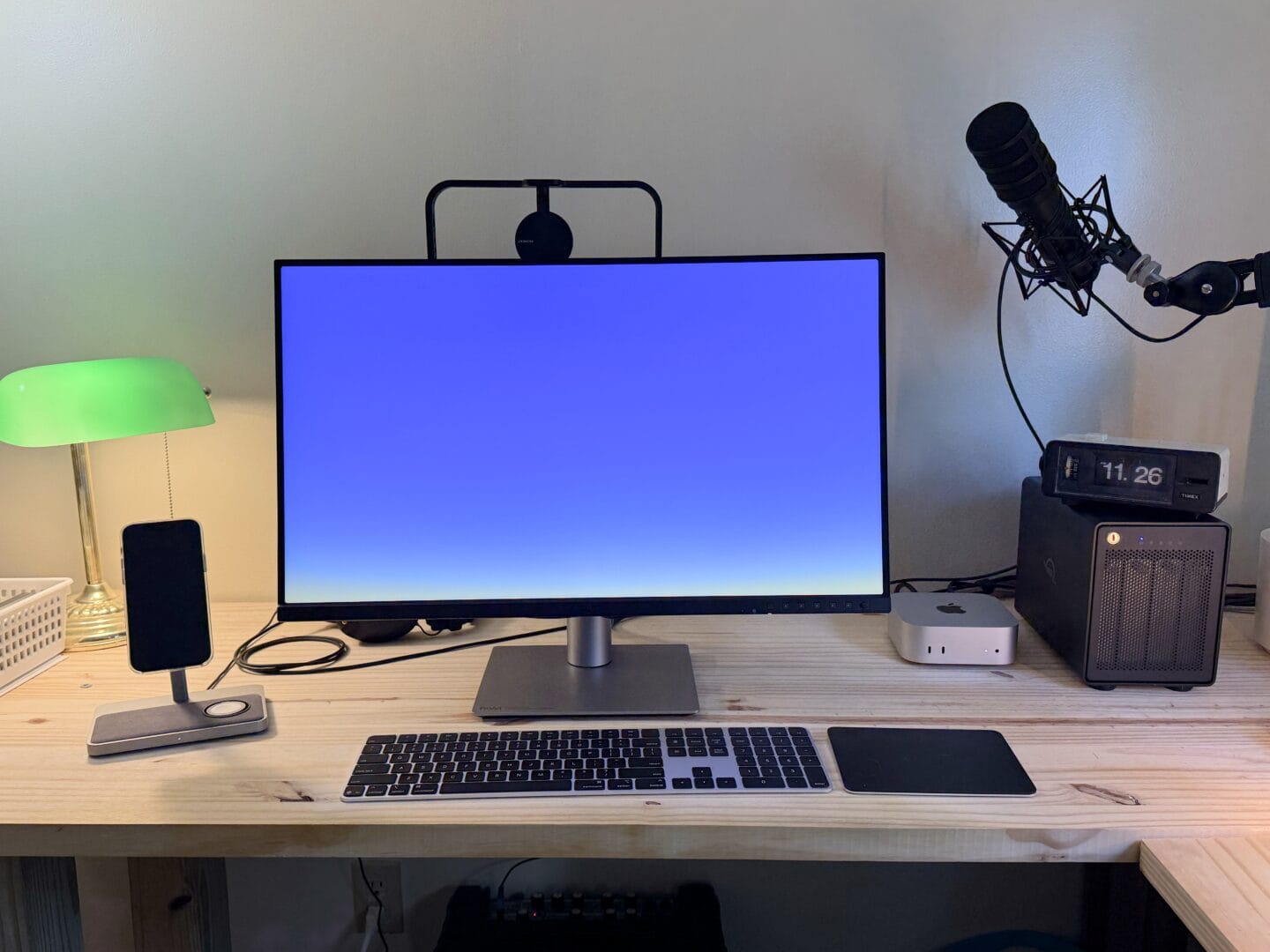 Mac mini setup with display, keyboard, trackpad, external storage, iPhone mount and podcasting microphone.