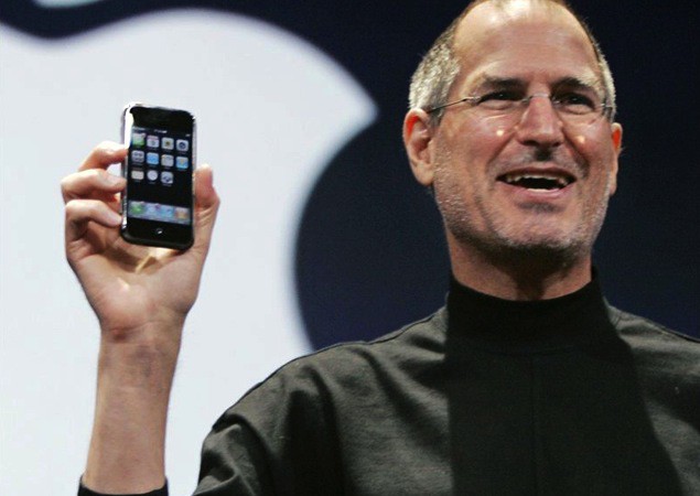 Photo of Steve Jobs holding an iPhone in front of an Apple logo during the first iPhone demo on January 9, 2007.